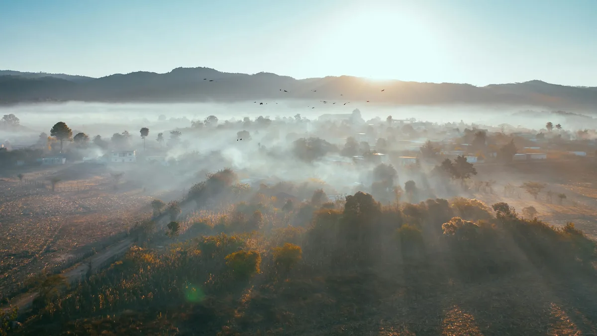 Dawn's warmth unfurls a misty veil, shrouding the valley's contours in mystery. Soft golden light creeps over the landscape…