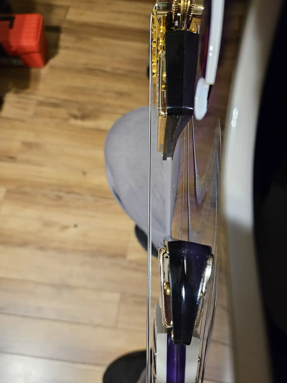 A close-up shot of a transparent-bodied electric bass guitar with gold hardware and purple accents, held vertically. The…