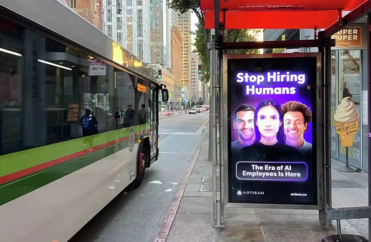 A bus stop advertisement displays a bold message: 'Stop Hiring Humans' above three smiling human faces, followed by 'The Era…