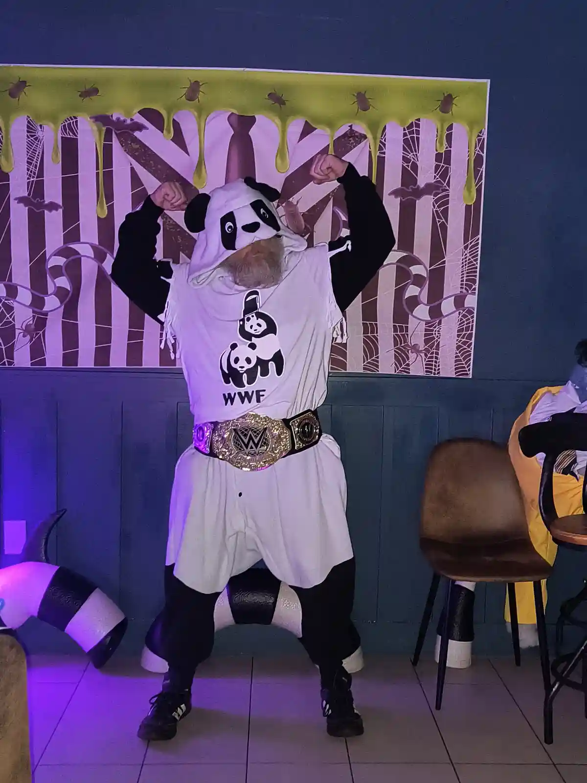 A man with a beard wears a panda-themed hoodie and a white t-shirt with a WWF logo and panda graphic, posing with flexed…