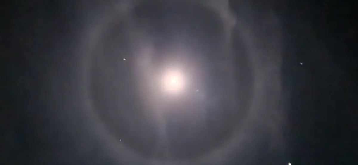 A bright light source, likely the sun, is surrounded by a thick, swirling ring of dark clouds or fog, creating a halo…