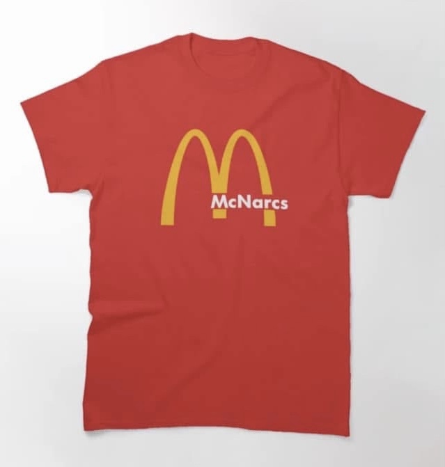 A red t-shirt displays the iconic golden arches logo of McDonald's, but the text beneath it is altered to read 'McNarcs'…