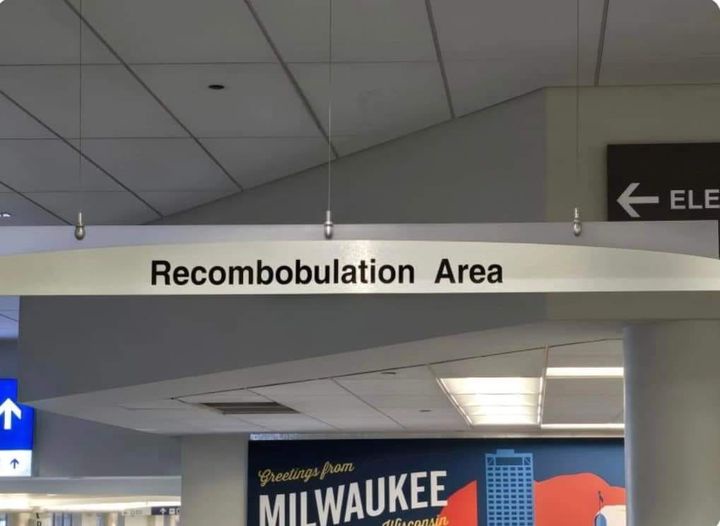 A photo of an airport or transit station sign that reads 'Recombobulation Area' in black text on a white background…