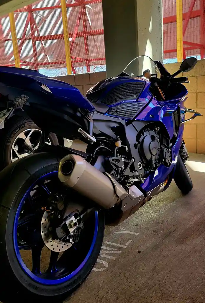 A shiny blue Yamaha sport motorcycle is parked in a garage with red and yellow safety netting in the background. The bike is…