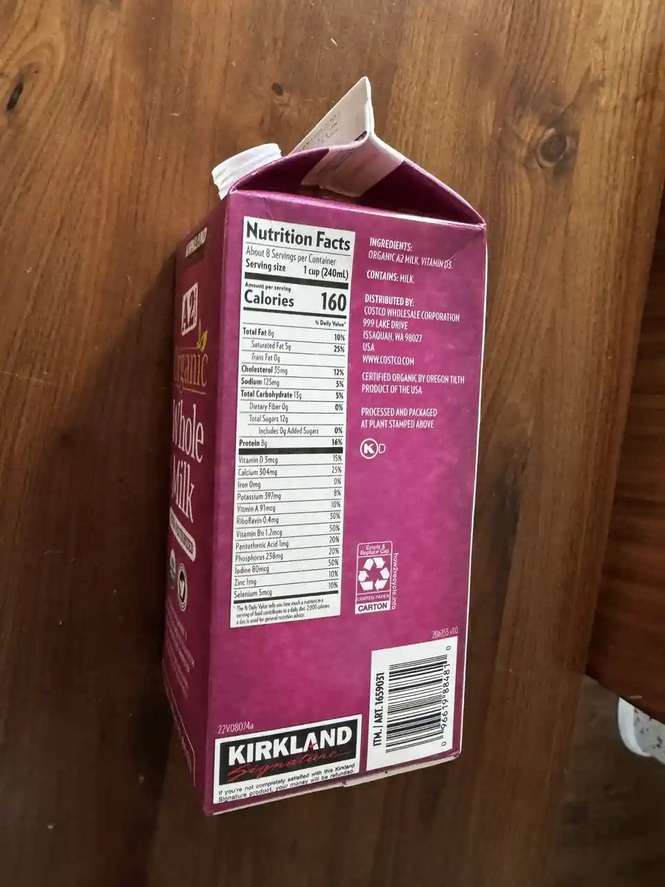 A purple Kirkland Signature organic whole milk carton, viewed from the back showing its nutrition facts label, ingredients…