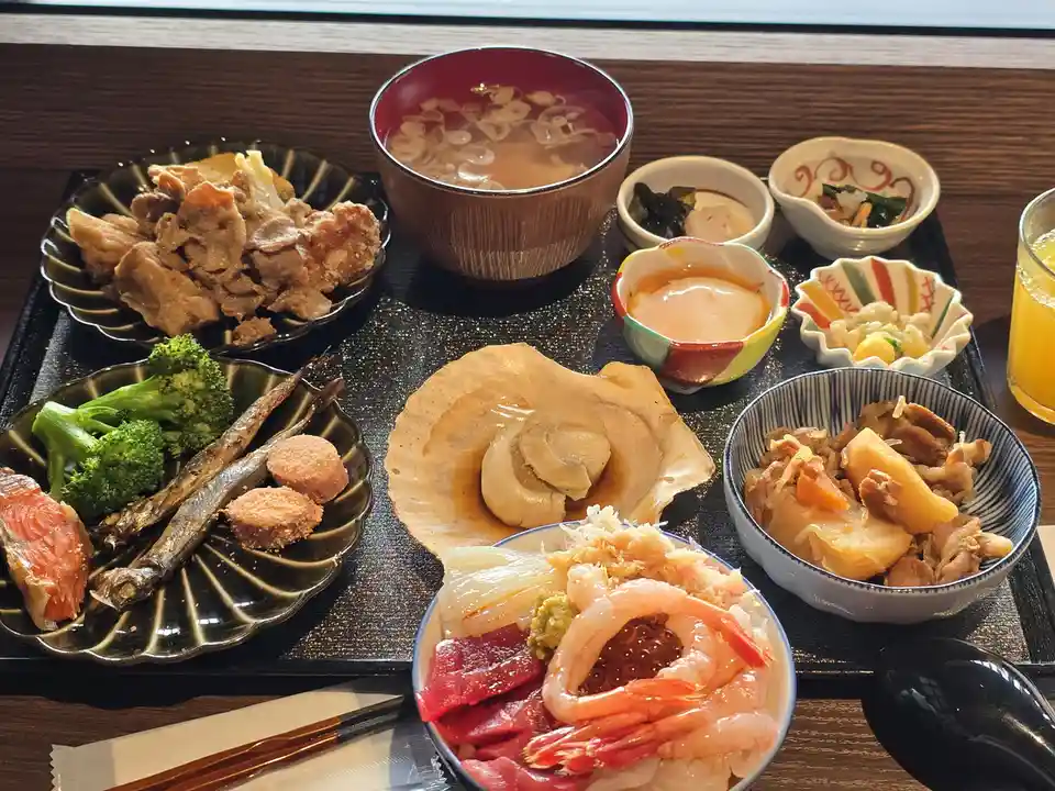 A lavish Japanese bento-style meal is presented on a black tray, featuring a large bowl of sashimi with shrimp and tuna, a…