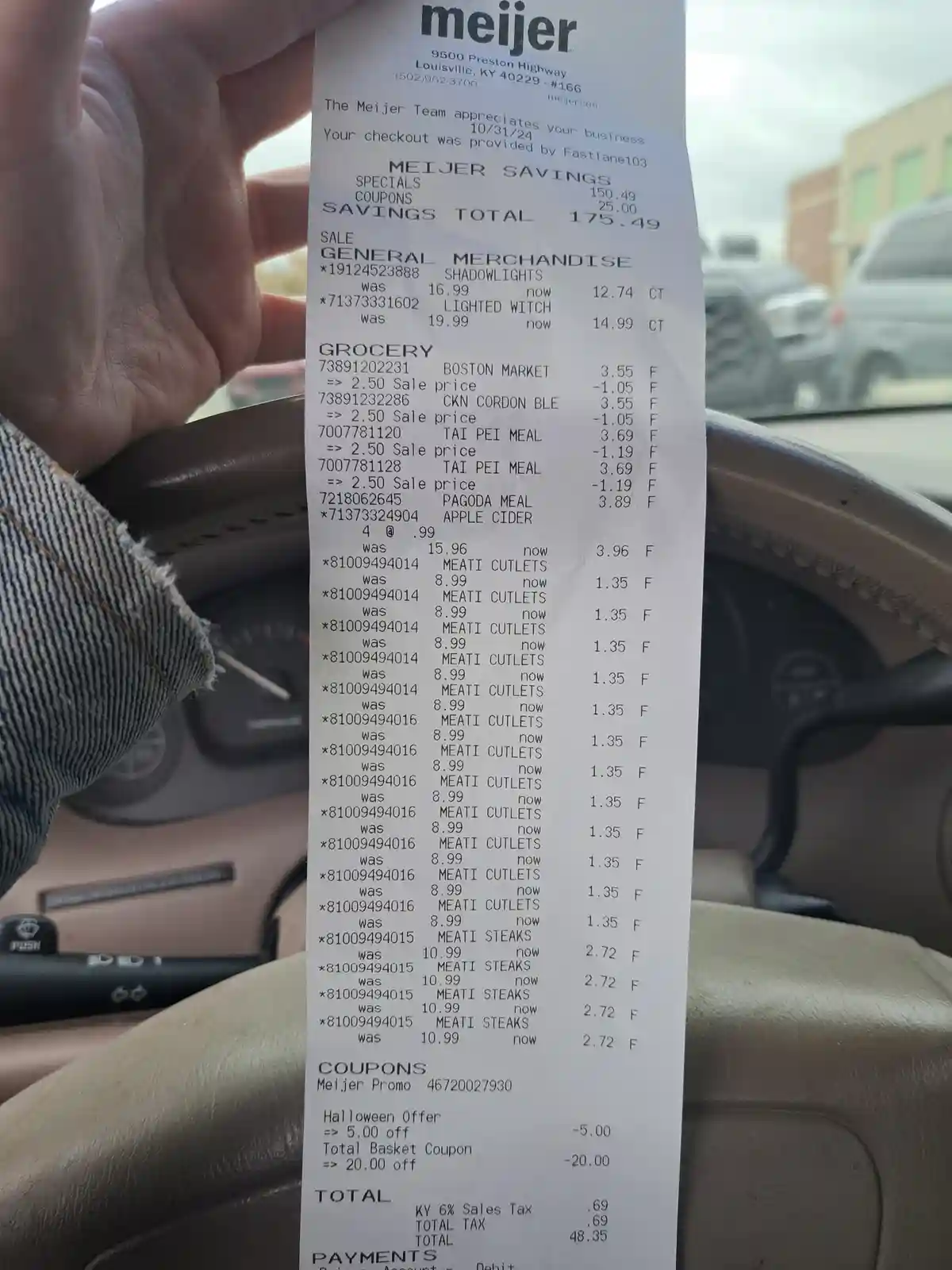 A close-up photo of a Meijer grocery receipt held inside a car, showing numerous items like 'LIGHTED WITCH' and 'MEATI…