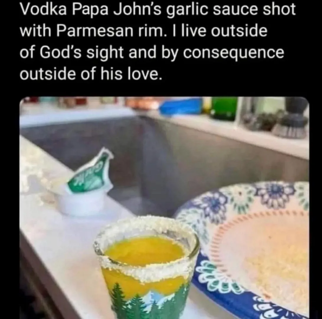 A close-up photo shows a shot glass filled with a yellow liquid, rimmed with grated Parmesan cheese, sitting on a kitchen…