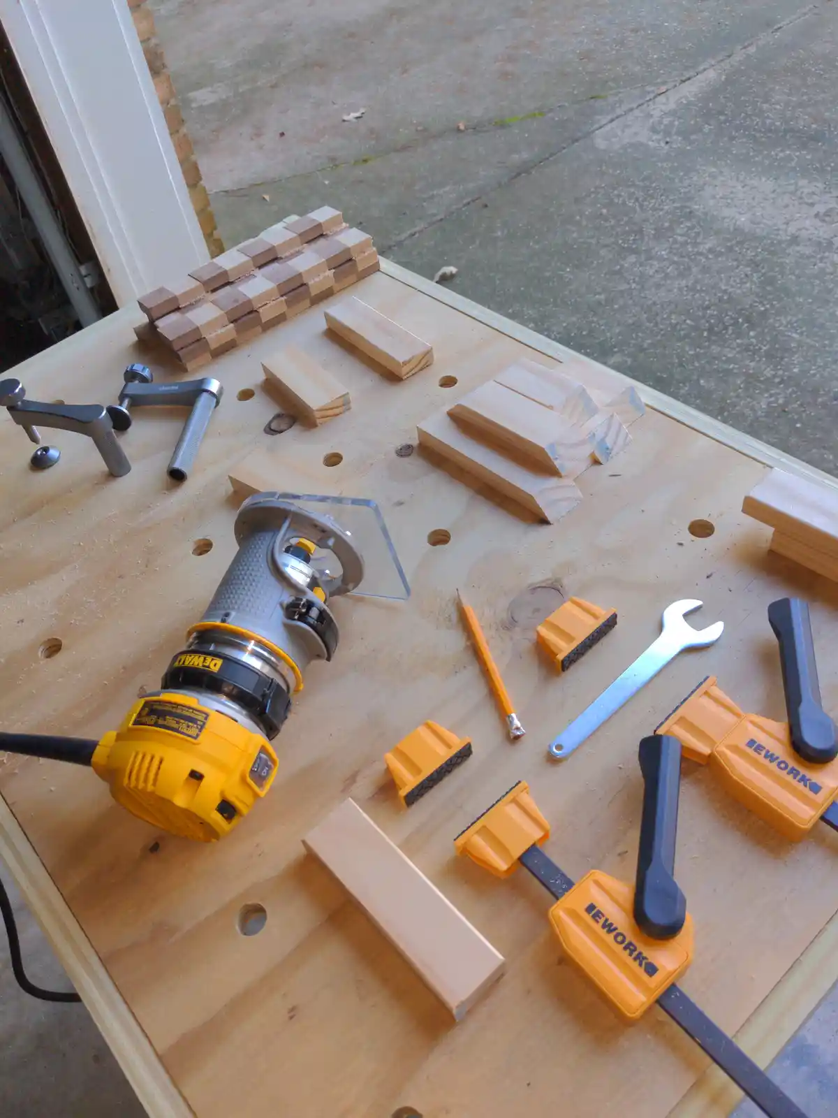 A wooden workbench is covered with woodworking tools including a yellow DeWalt router, orange clamps, a wrench, and a…