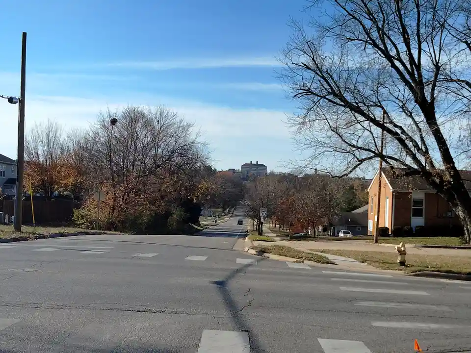 A photo of a quiet suburban street with bare trees and a distant building under a blue sky, overlaid with the text 'i'm not…