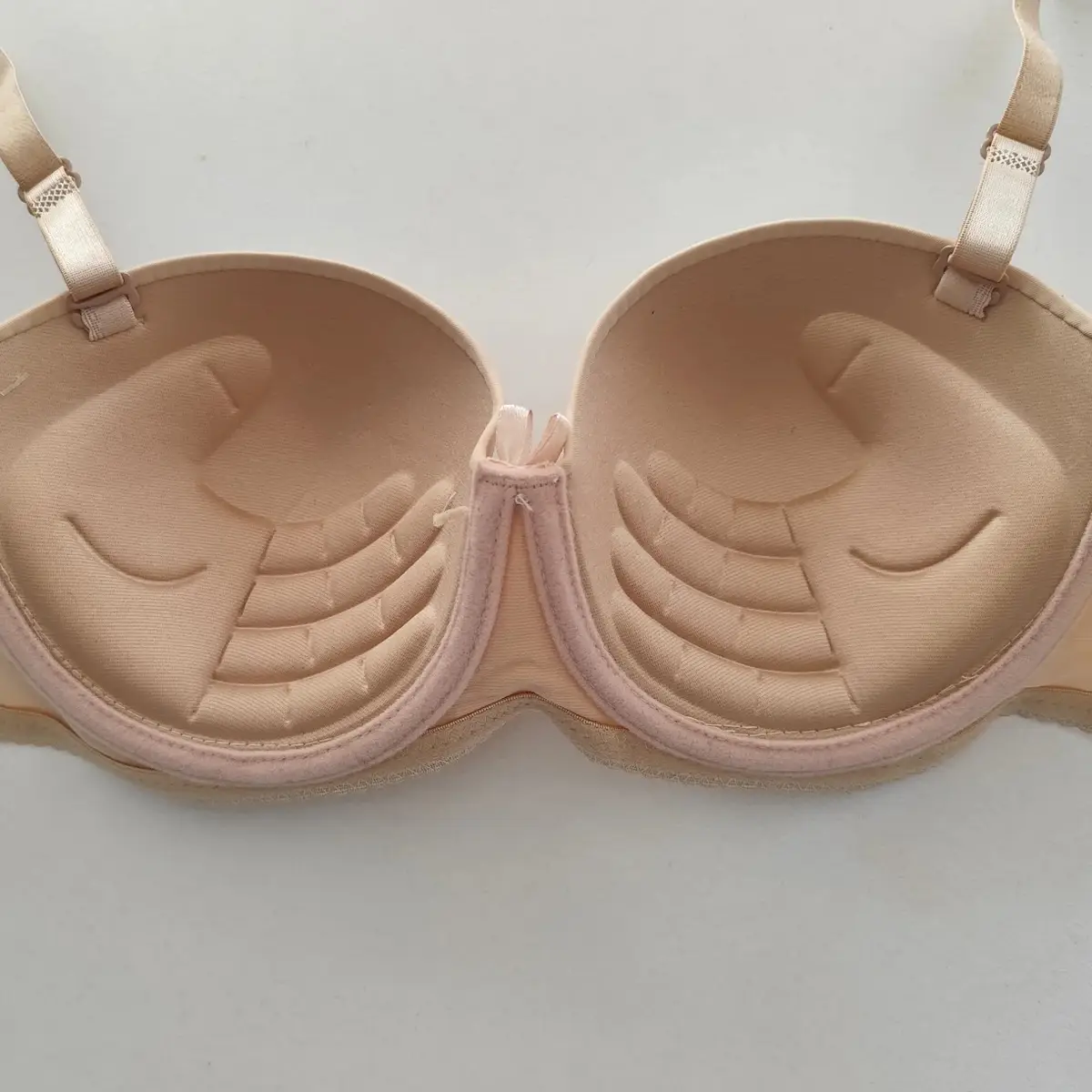 A light pink, strapless bra is laid flat, showing its inner cups which have molded smiley faces with curved eyes and mouths…