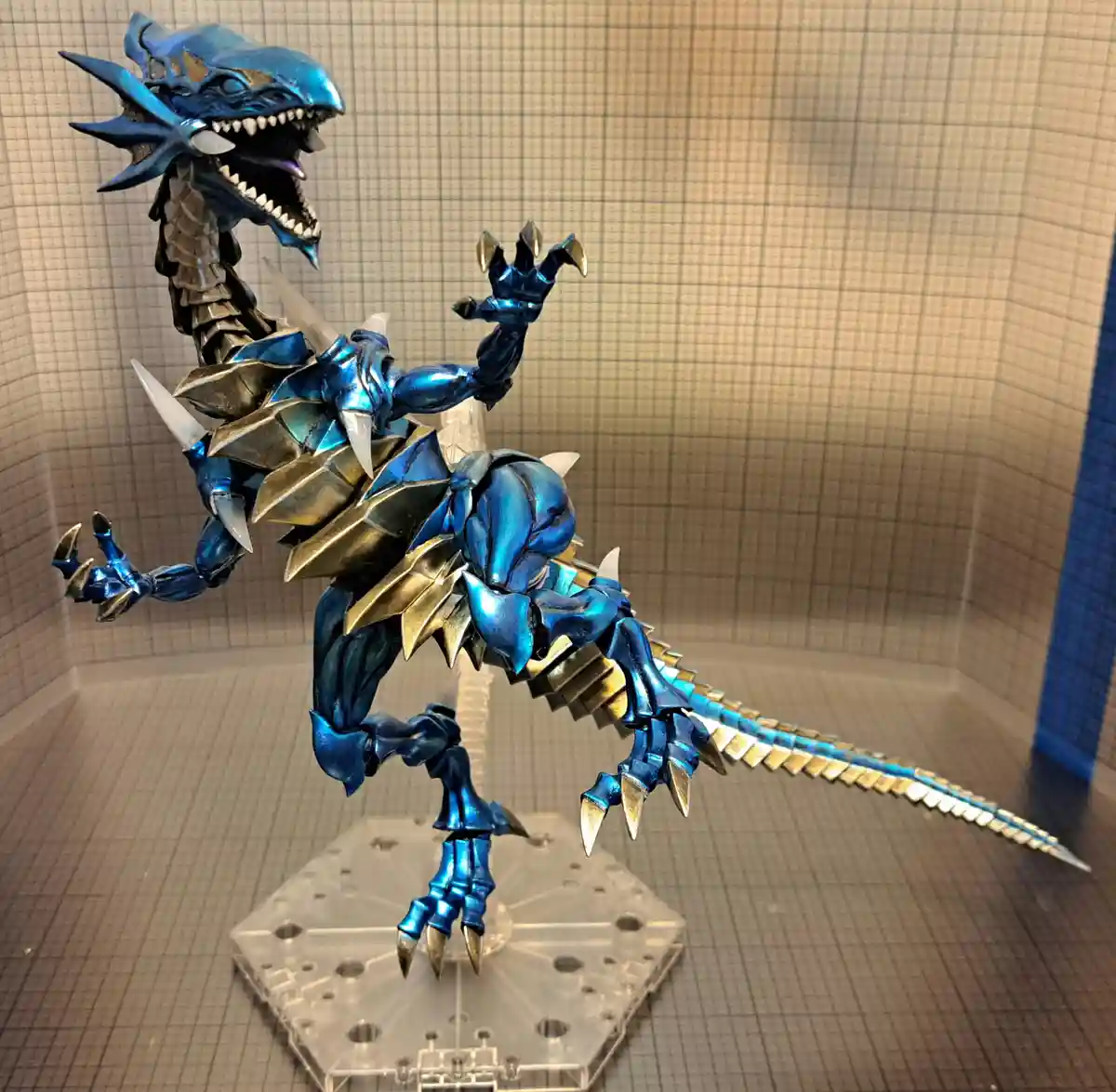 A highly detailed, metallic blue and gold dragon figure with sharp claws and teeth, posed dynamically on a clear plastic…