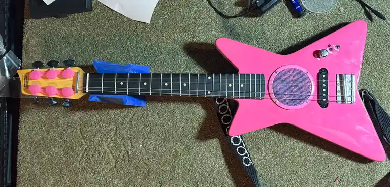 A bright pink, star-shaped toy electric guitar with a built-in speaker and volume/phone jack, branded 'First Act Discovery'…
