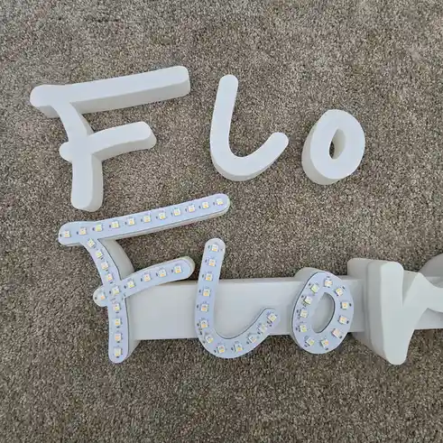 The image shows the word 'Flo' spelled out with white, three-dimensional letters on a beige carpet. The top row displays the…