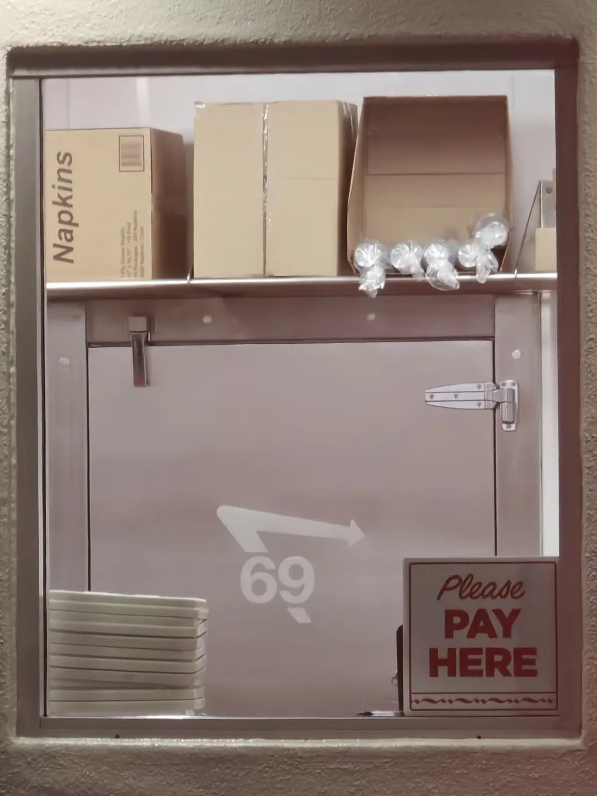 A metal service window with a frosted glass door showing a large white arrow pointing right and the number 69 below it. On…