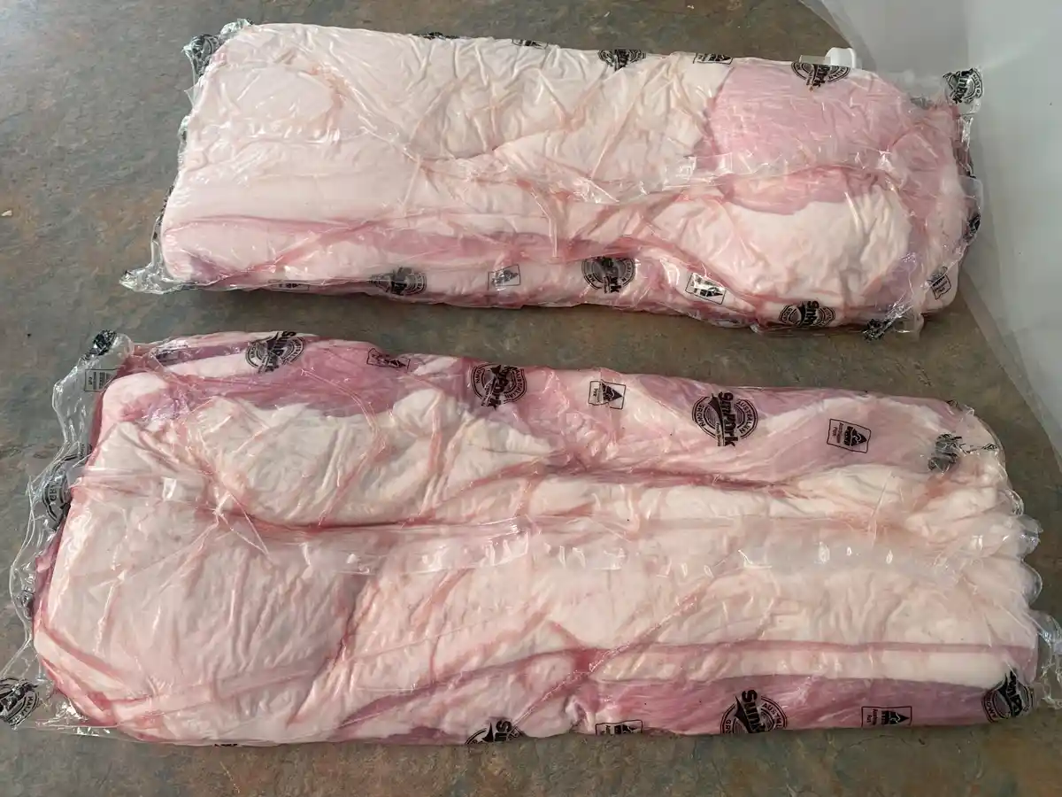 Two large, vacuum-sealed packages of raw pork belly meat, each wrapped in clear plastic with 'Sun Pork' branding visible…