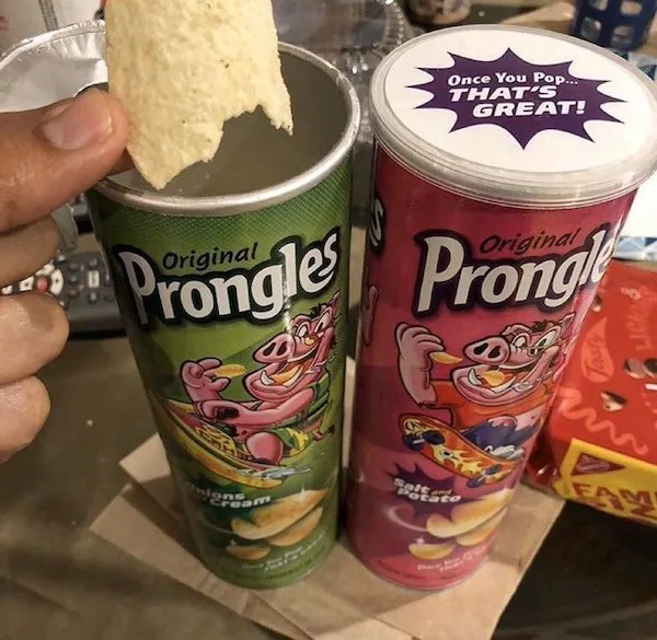 Two Pringles cans, one green 'Onions & Cream' and one red 'Salt & Potato', sit side by side. A hand holds a partially eaten…