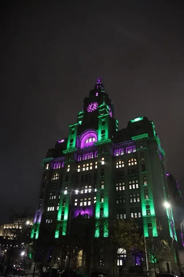 a nighttime photograph of the iconic liverpool cathedral, its facade illuminated with vibrant green and purple lights along…