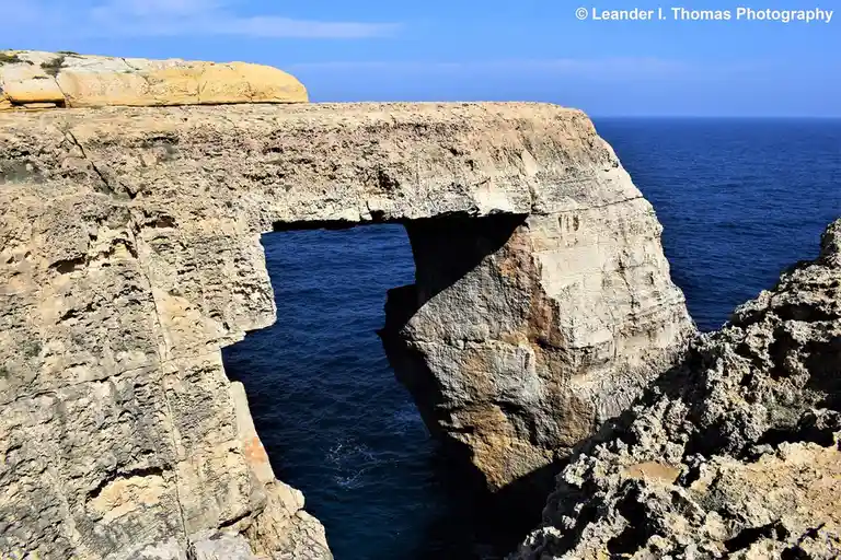 A natural rock arch formation over a deep blue sea under a clear sky, with overlaid text reading 'blue hole'. The image…