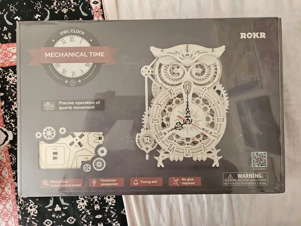 A product box for a ROKR brand owl-shaped mechanical clock kit, featuring a detailed illustration of the assembled clock…