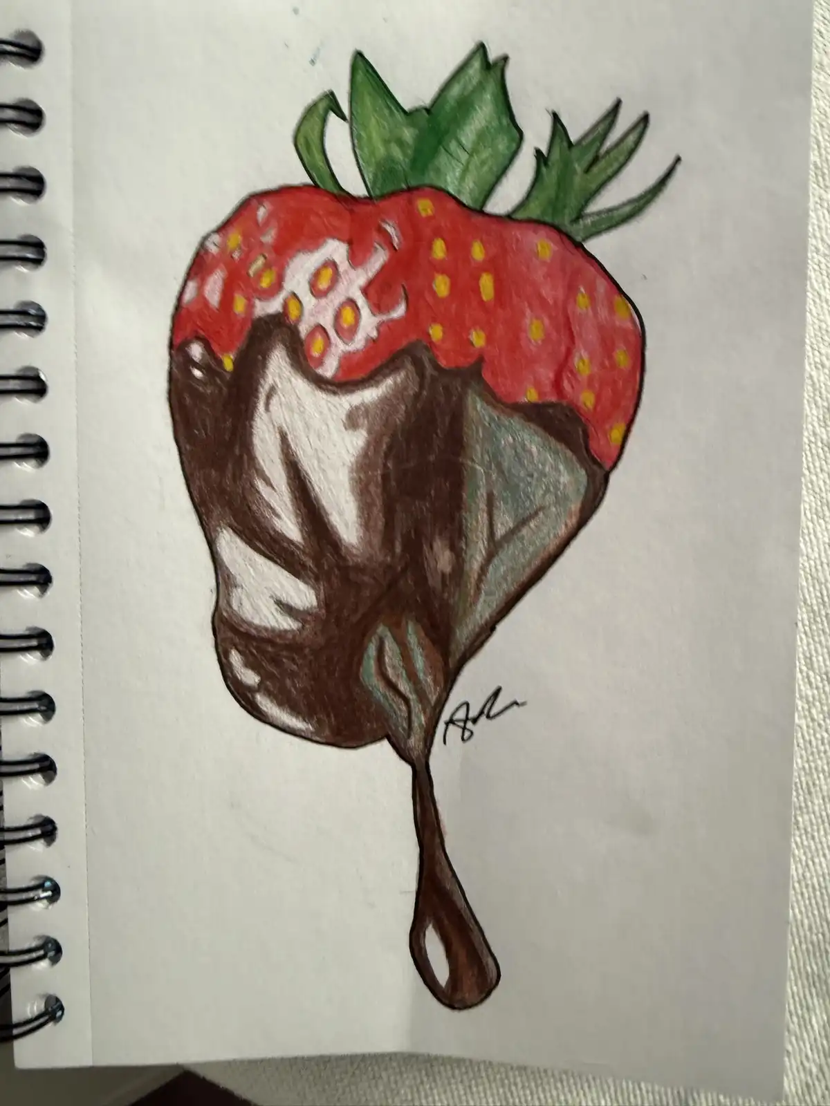 A hand-drawn colored pencil illustration on spiral-bound notebook paper shows a strawberry with green leaves, half-coated in…