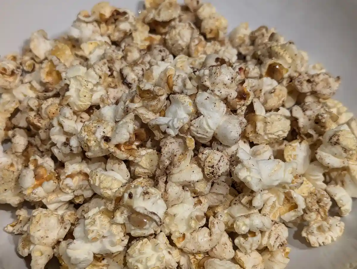 A close-up photo shows a pile of caramel-coated popcorn sprinkled with dark specks, likely cocoa or spice, resting in a…