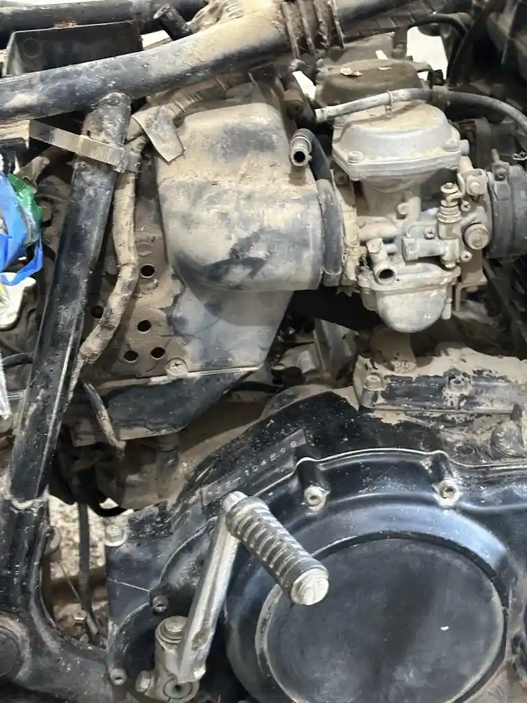 A close-up photo of a very dirty and dusty motorcycle engine, showing components like the carburetor, air filter housing…