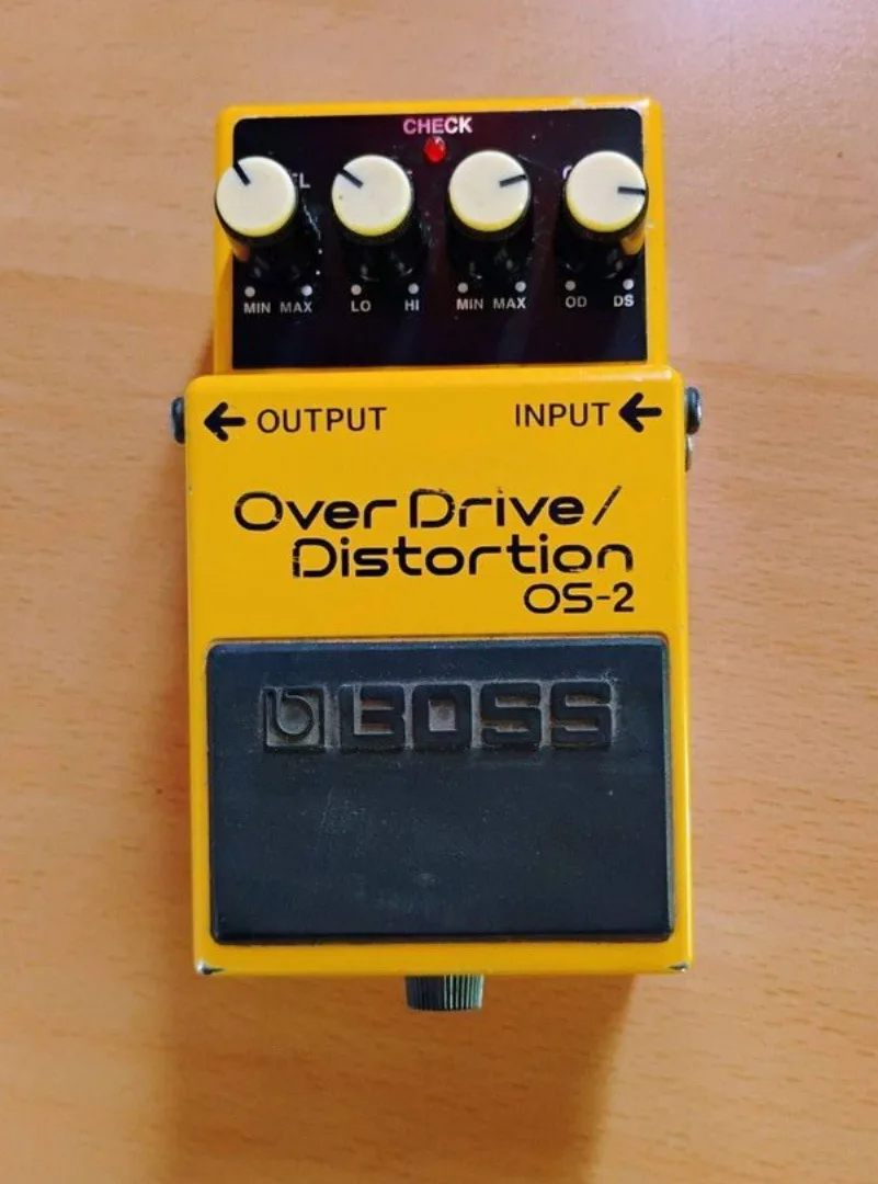 A yellow Boss OS-2 Over Drive/Distortion guitar effects pedal with four knobs and a black footswitch, sitting on a wooden…
