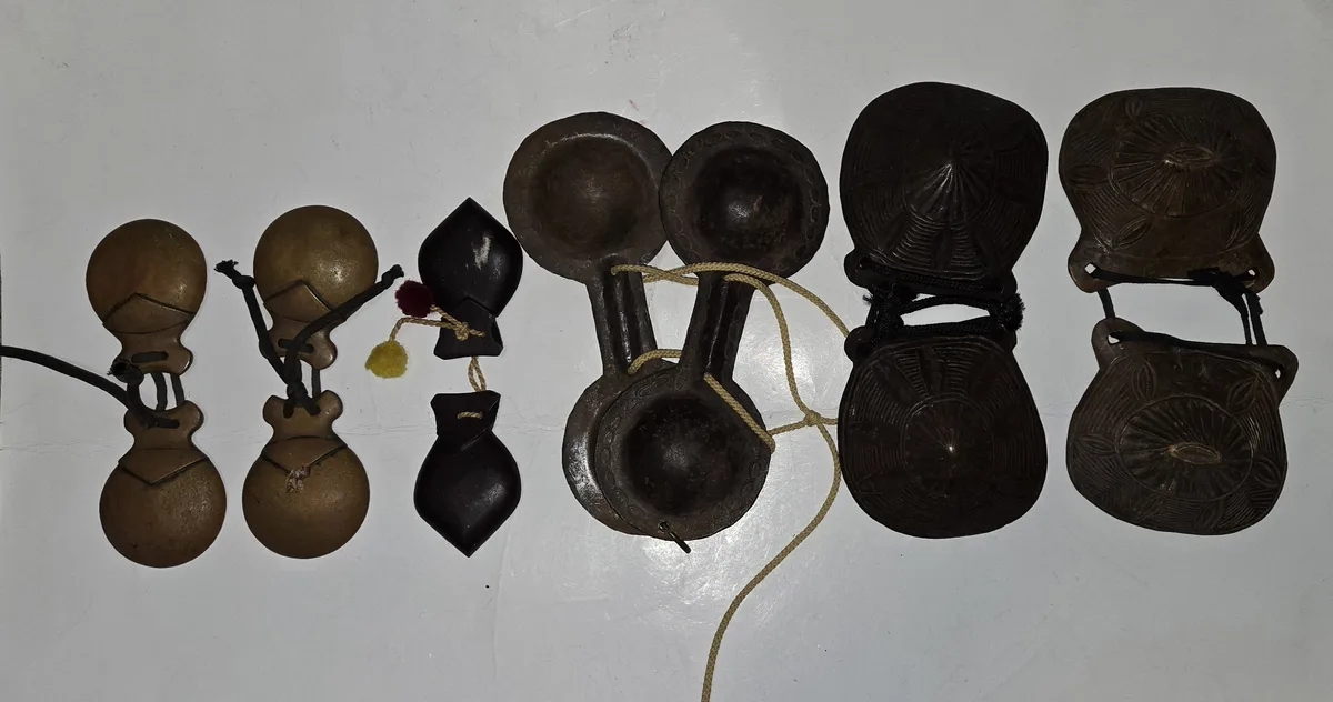 A row of various traditional hand bells and clappers, including brass and dark wooden ones with intricate carvings, are laid…