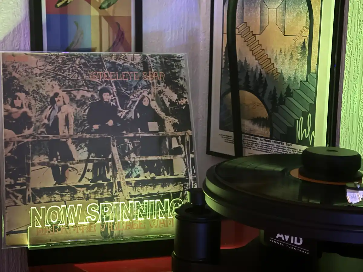 A vinyl record player with a green-lit turntable is shown next to a standing album cover for 'Steeleye Span' with the text…
