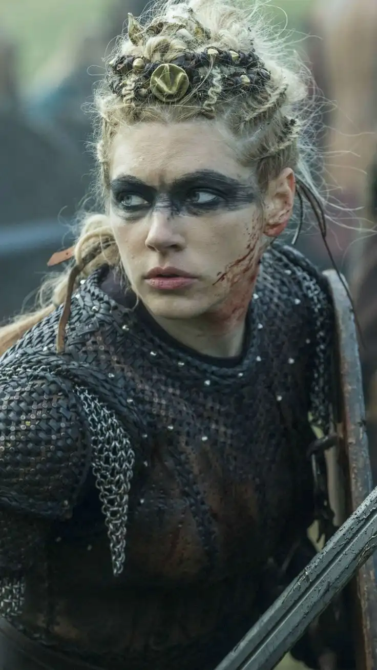 A woman in battle armor with a bloodied face and dark eye makeup looks sideways with a skeptical expression. She wears a…