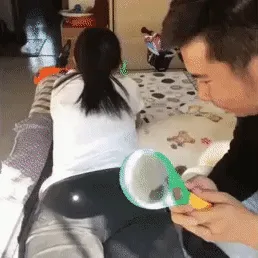 A man holds a small hand mirror and examines a woman's backside while she sits on a couch. In the next frames, the woman…