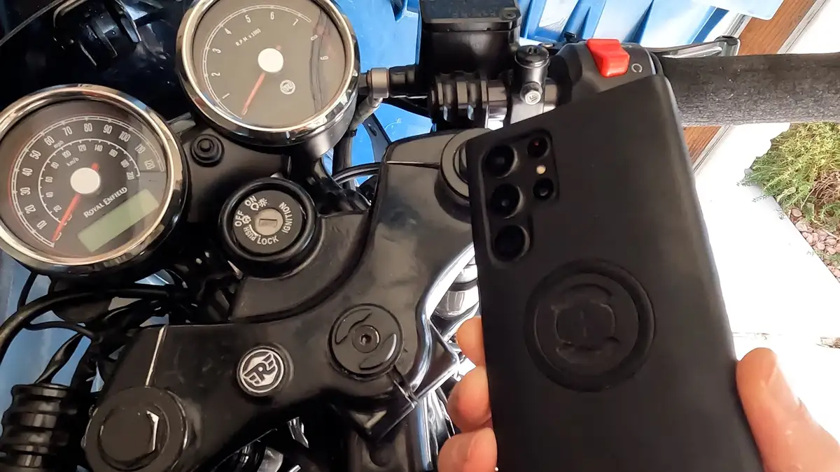 A close-up photo shows a hand holding a black smartphone with a multi-lens camera array, positioned directly in front of a…
