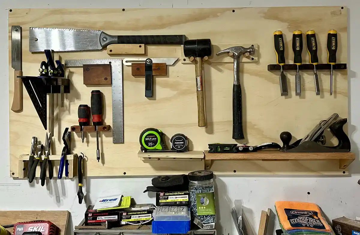 A well-organized wooden wall-mounted tool rack displays various woodworking and construction tools including hammers…