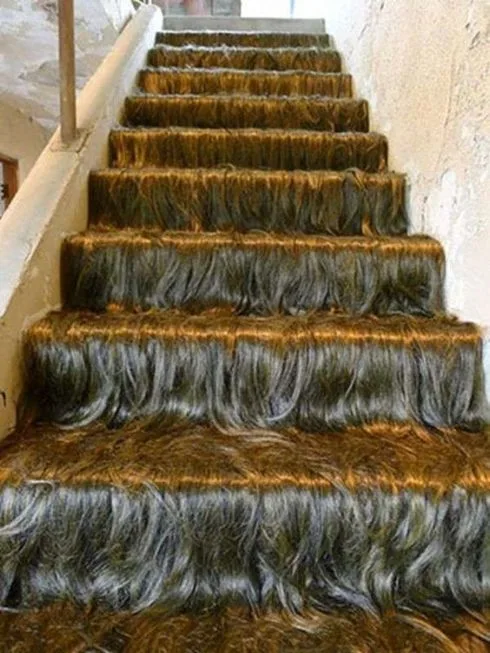 A staircase is covered in long, dark, wavy hair, arranged in thick rows on each step, creating a textured, layered…