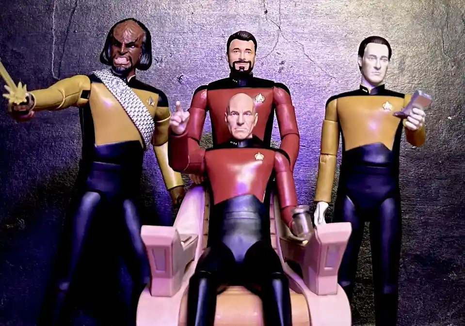 three star trek action figures are posed: a figure in a red uniform sits in a captain's chair with a bald head, flanked by…