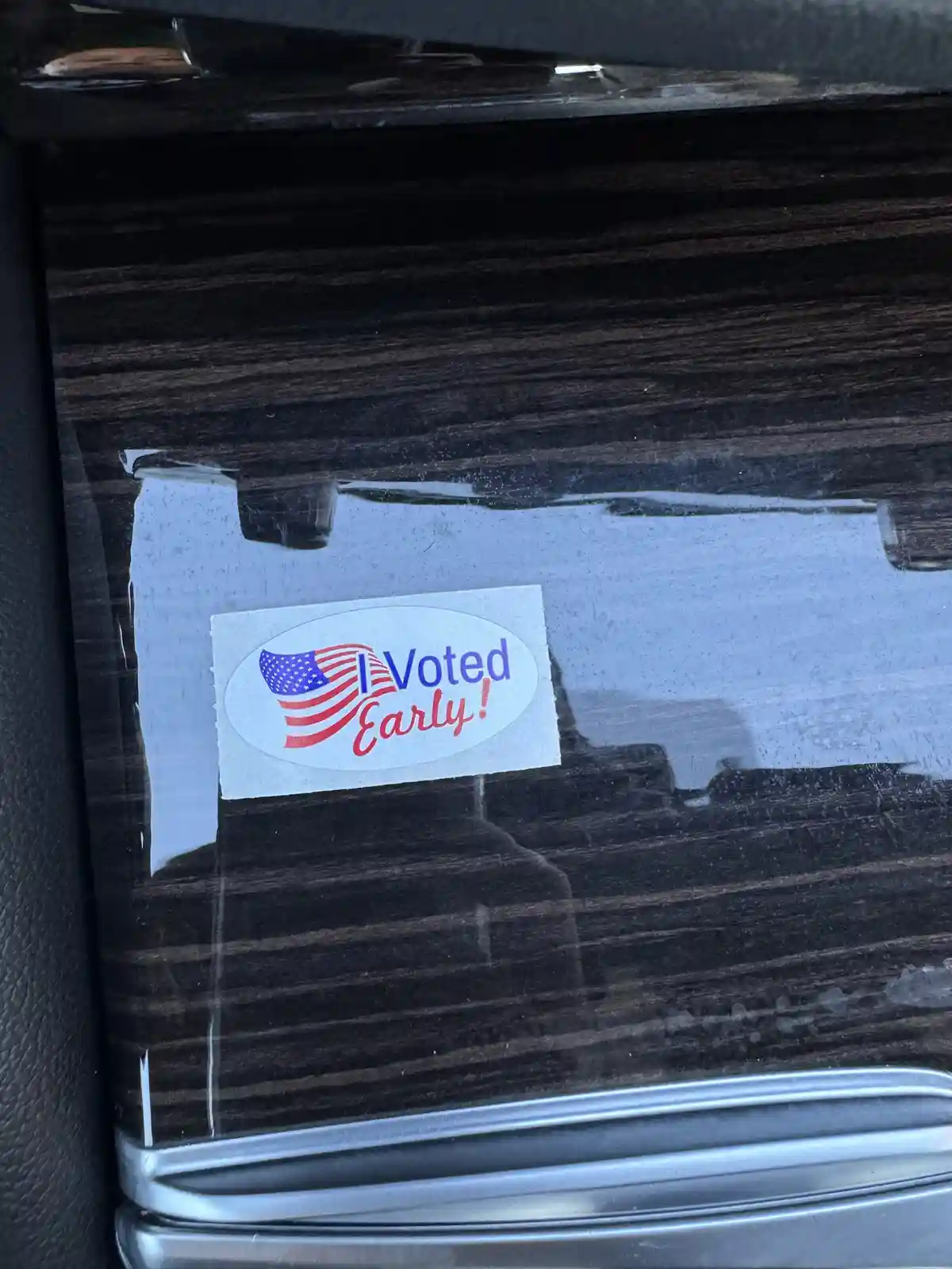 A close-up photo shows an 'I Voted Early!' sticker with a stylized American flag design, affixed to the rear window of a car…
