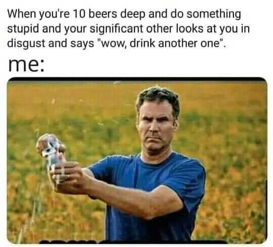 A man in a blue t-shirt stands in a field, holding a beer bottle and pouring it with a disgusted, intense facial expression…