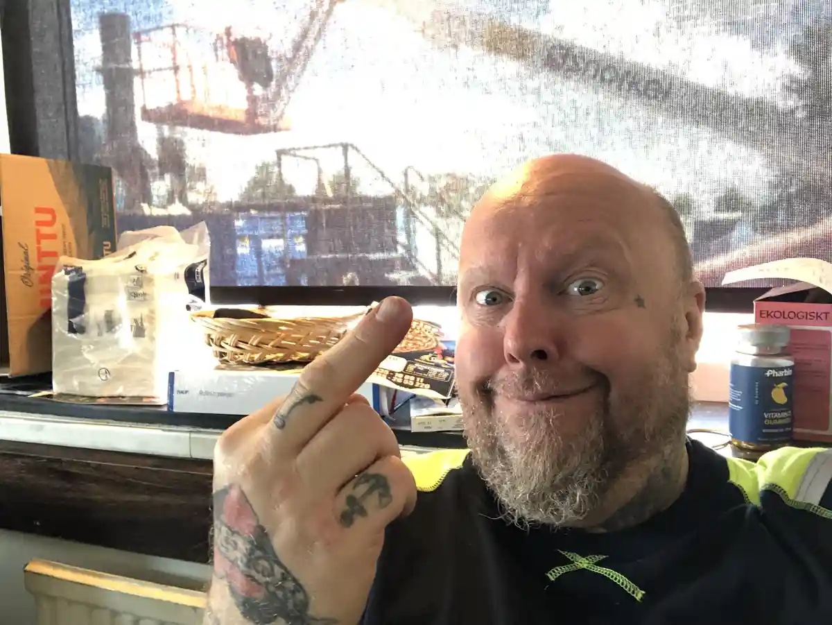 A bald man with a grey beard and tattoos on his hand and neck points his index finger at the camera with a smug, knowing…