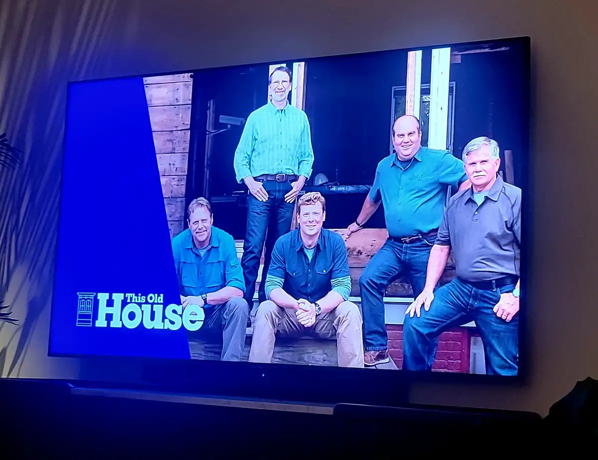 A television screen displays the promotional image for the show 'This Old House,' featuring five men in work clothes posing…