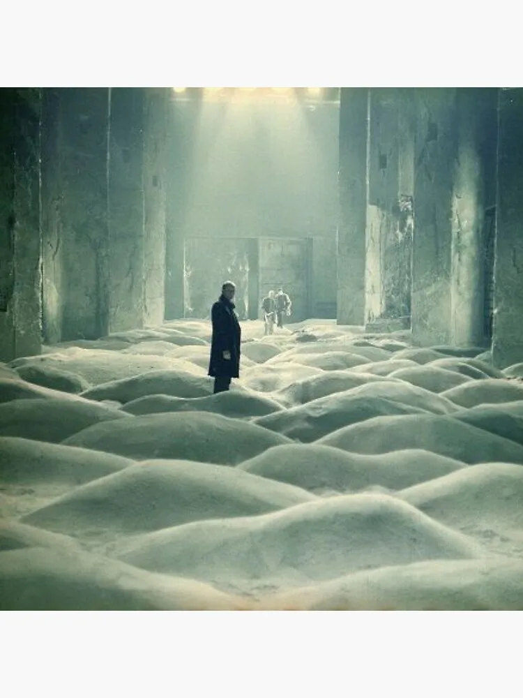 A person stands alone in a vast, dimly lit, abandoned hall covered in mounds of white material resembling snow or sand. In…