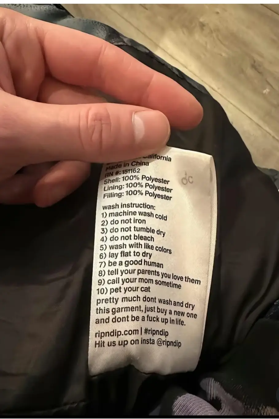 A close-up photo shows a hand holding a clothing care label from a black jacket, which lists standard fabric composition and…