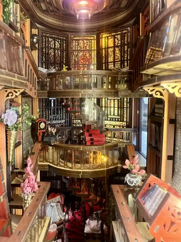 A highly detailed, multi-level miniature dollhouse library with wooden balconies, bookshelves, and decorative elements like…