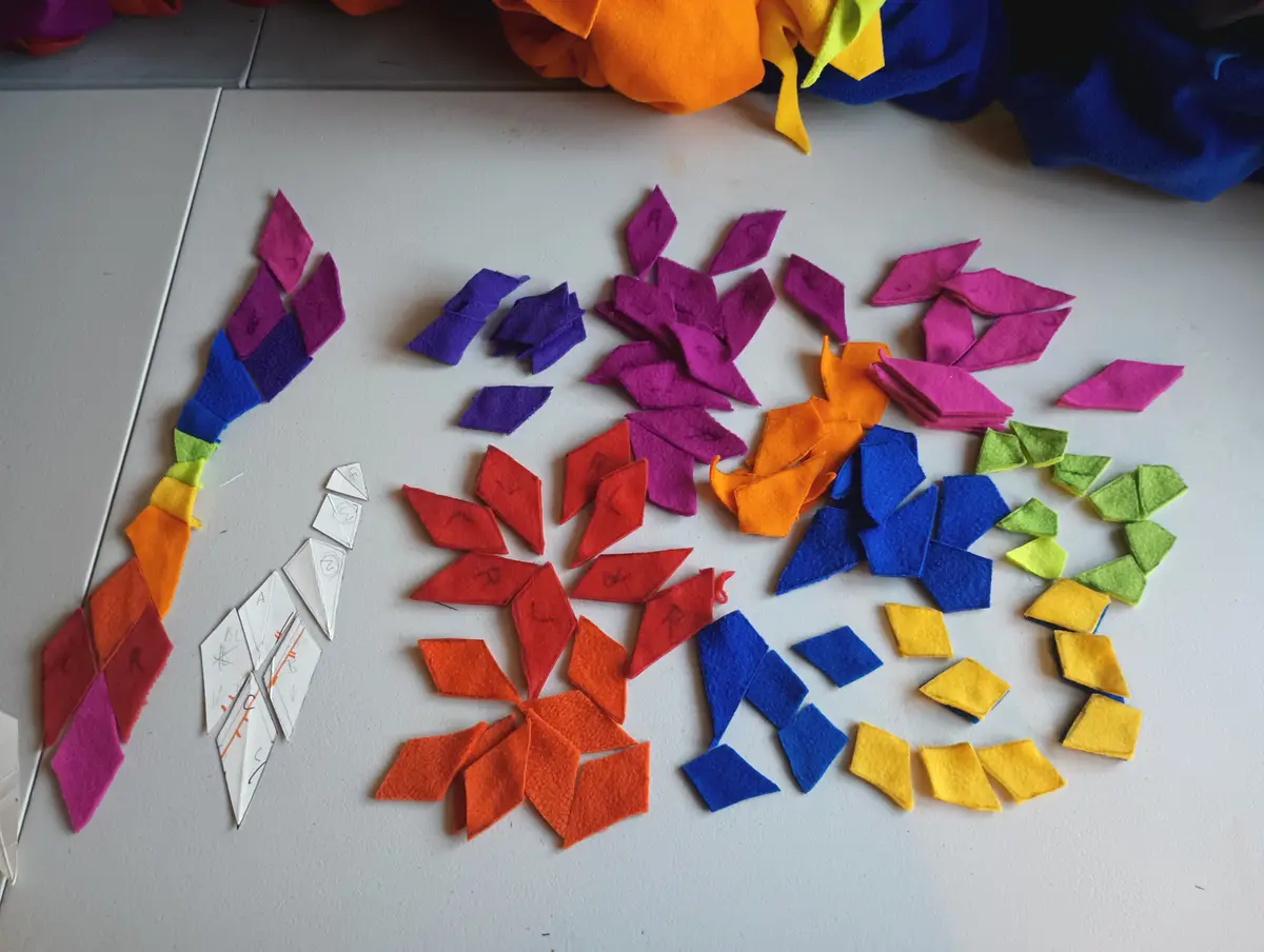 A white tiled surface is covered with colorful felt pieces arranged in rainbow order, with some pieces already assembled…
