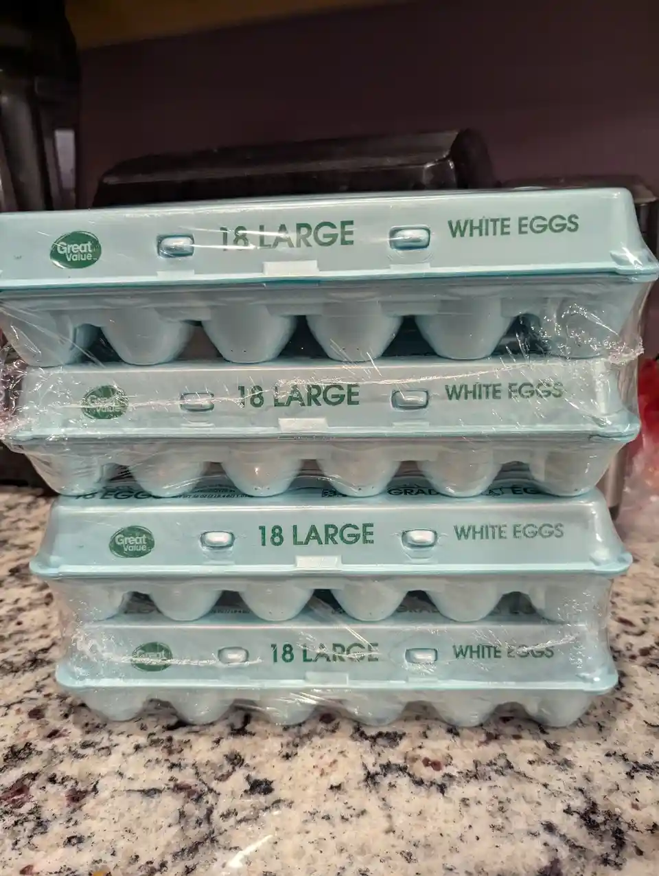 Four identical light blue 'Great Value' brand egg cartons, each labeled '18 LARGE WHITE EGGS', are stacked vertically on a…
