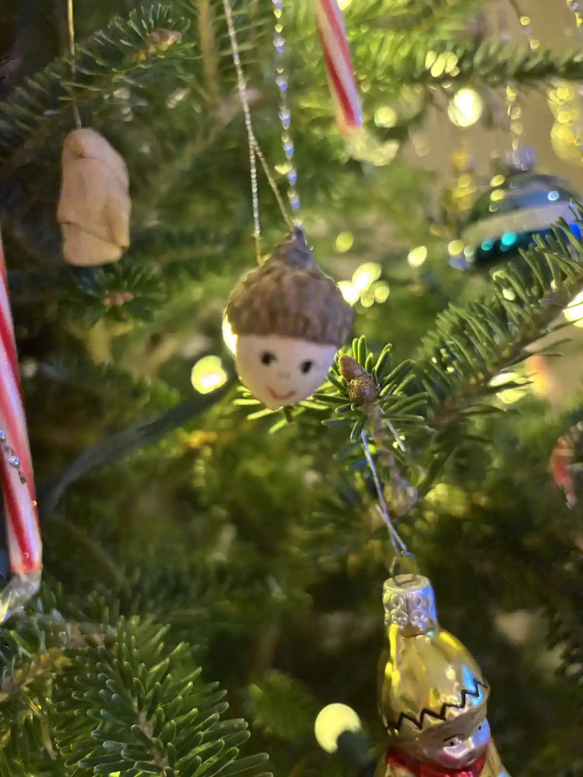 A close-up of a decorated Christmas tree with various ornaments, including a small, smiling figurine with a brown acorn cap…