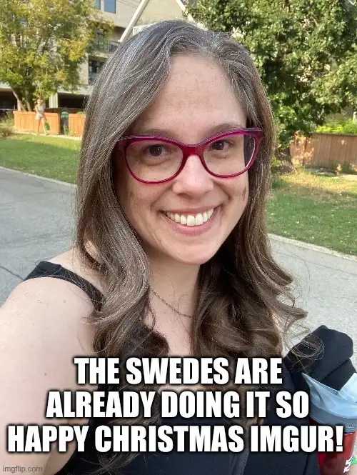 A woman with long brown hair and red glasses smiles at the camera outdoors. White bold text overlaid at the bottom reads…