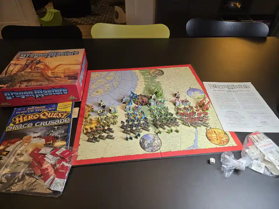 A tabletop setup of the Dragon Masters fantasy board game, featuring a large map with numerous miniature armies in blue…