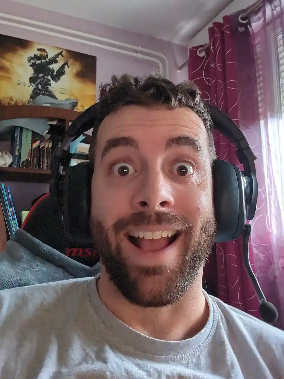 A man with a beard and headphones stares at the camera with wide eyes and an open mouth, conveying extreme shock or…