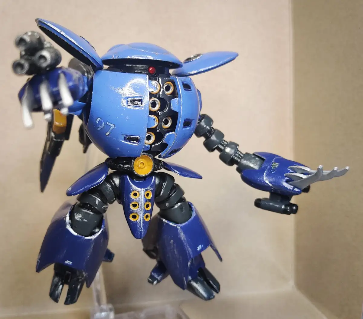 A blue, custom-painted robot model with exposed internal wiring and mechanical parts, standing on a clear stand against a…